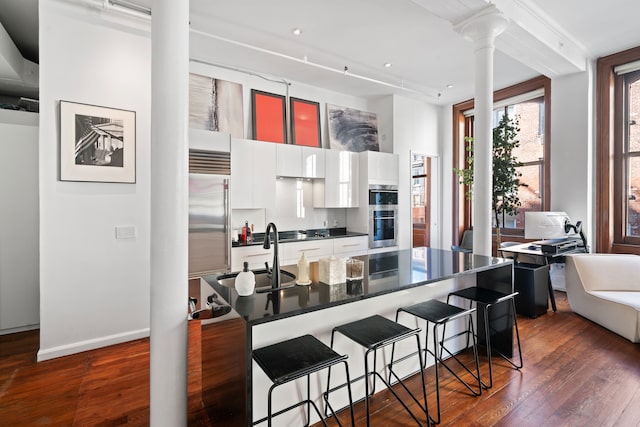 kitchen featuring dark countertops, a sink, a kitchen bar, white cabinets, and dark wood-style flooring