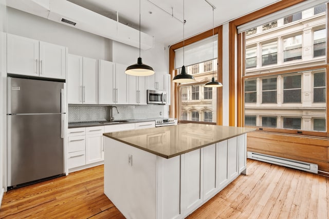 kitchen with a baseboard radiator, decorative backsplash, appliances with stainless steel finishes, white cabinetry, and a sink