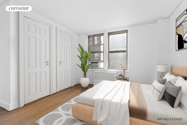 bedroom featuring visible vents, baseboards, radiator heating unit, cooling unit, and wood finished floors