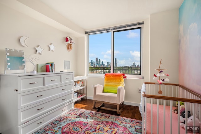 bedroom with dark wood-style flooring, a skyline view, a nursery area, and baseboards