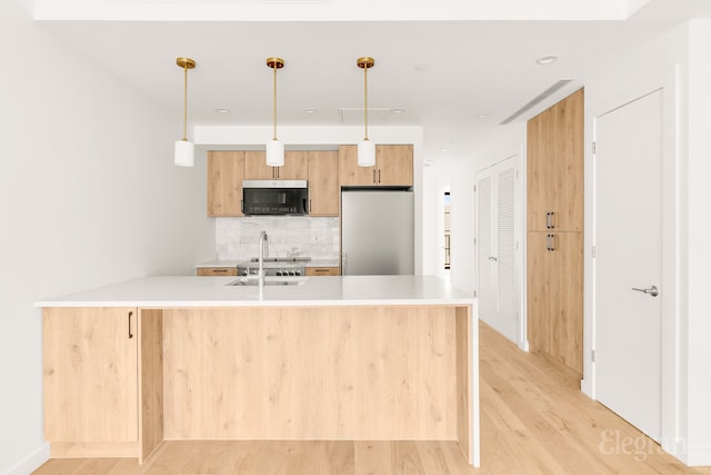 kitchen featuring a sink, stainless steel fridge, light wood-style floors, light countertops, and decorative backsplash