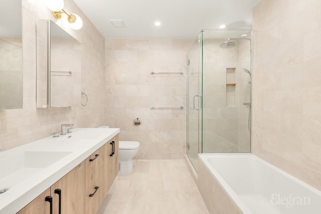 bathroom featuring tiled shower, double vanity, a sink, tile walls, and toilet