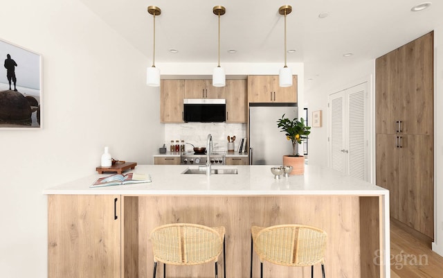 kitchen featuring decorative backsplash, a peninsula, stainless steel fridge, and light countertops