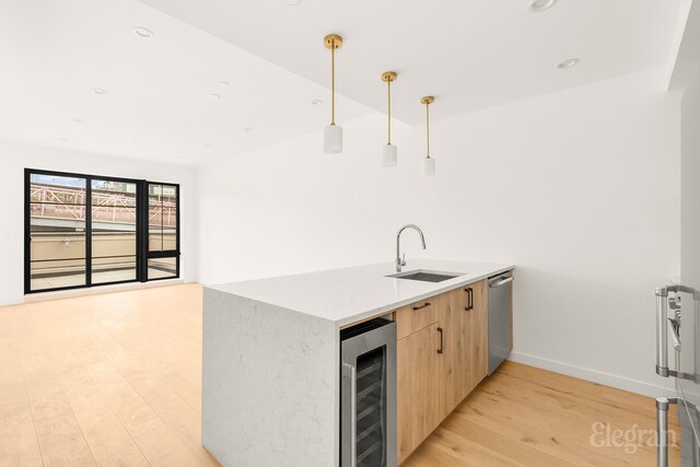 kitchen featuring beverage cooler, light brown cabinets, a sink, decorative light fixtures, and light wood finished floors