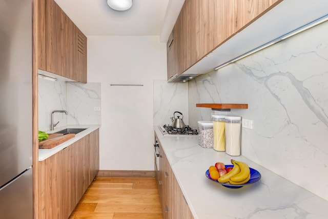 kitchen with light wood finished floors, appliances with stainless steel finishes, brown cabinetry, modern cabinets, and a sink