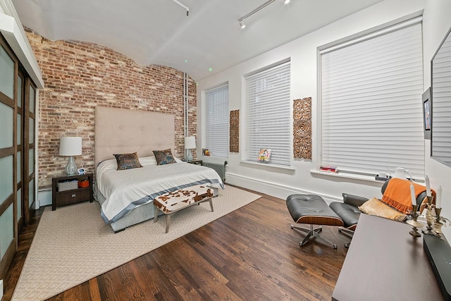 bedroom with wood finished floors, baseboards, brick wall, vaulted ceiling, and rail lighting