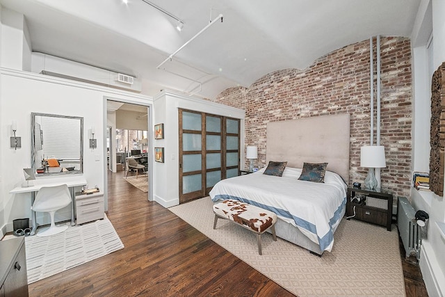 bedroom featuring brick wall, rail lighting, baseboards, and wood finished floors