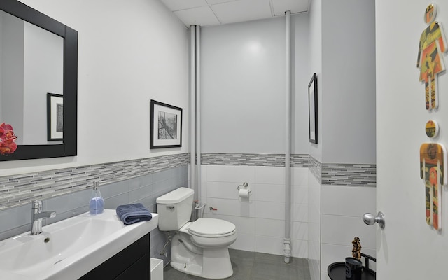 bathroom featuring tile patterned flooring, a drop ceiling, toilet, vanity, and tile walls