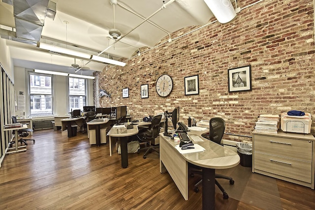 office area featuring dark wood-type flooring and brick wall