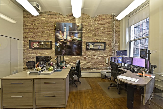 office with built in desk, dark wood finished floors, and brick wall