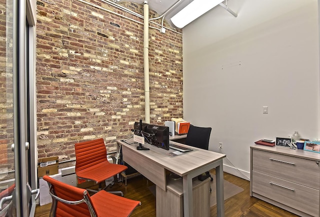 home office featuring dark wood-type flooring, baseboards, and brick wall