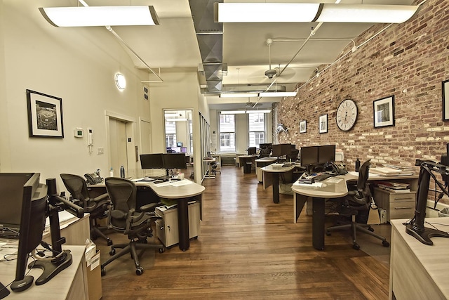 office space with a high ceiling, wood finished floors, and brick wall