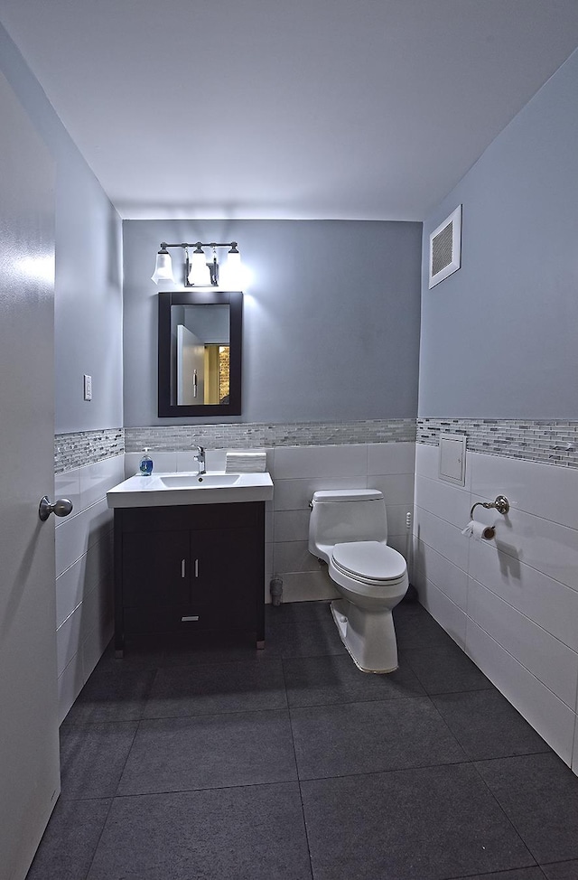 bathroom with visible vents, tile walls, a wainscoted wall, toilet, and vanity