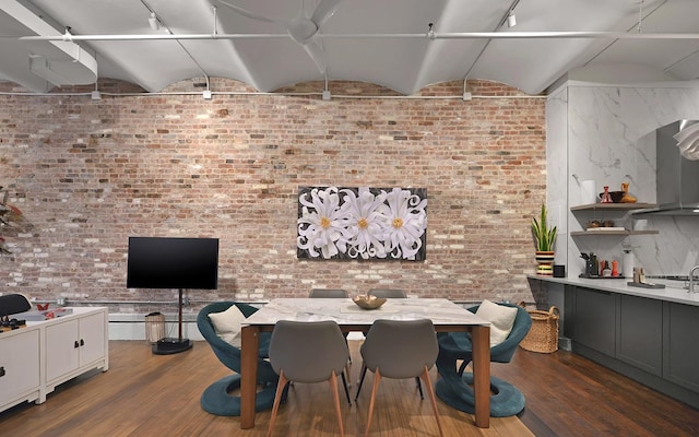 dining area with vaulted ceiling, brick wall, and wood-type flooring