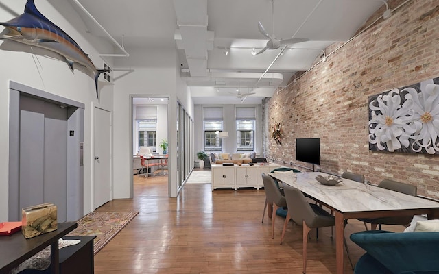 dining room featuring wood-type flooring, elevator, brick wall, and a towering ceiling