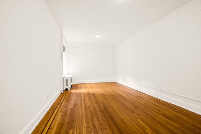 empty room featuring baseboards, wood-type flooring, and radiator