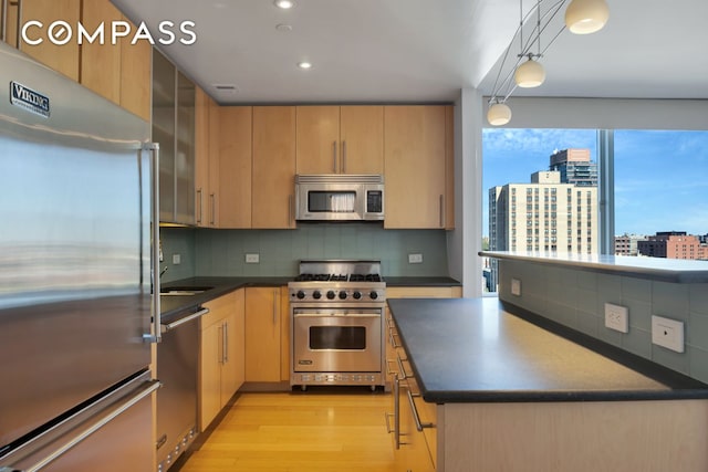 kitchen featuring dark countertops, high quality appliances, light brown cabinets, and light wood finished floors