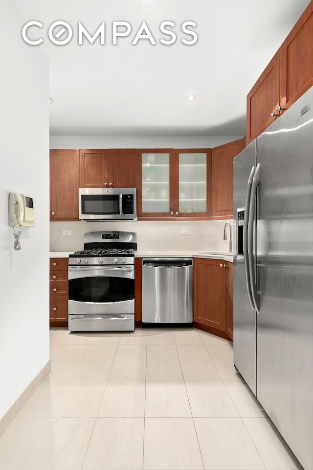 kitchen featuring light tile patterned floors, a sink, stainless steel appliances, light countertops, and glass insert cabinets