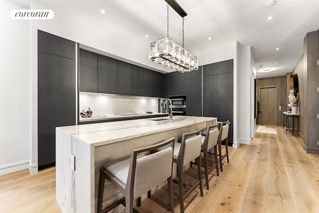 kitchen featuring a large island, modern cabinets, a sink, light wood-style floors, and dark cabinets