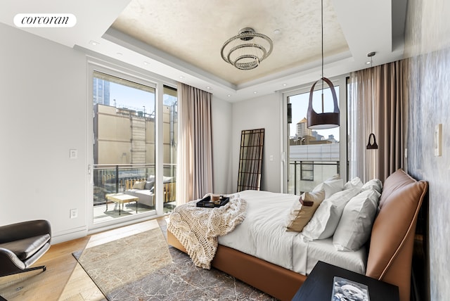 bedroom featuring access to exterior, visible vents, baseboards, wood finished floors, and a raised ceiling