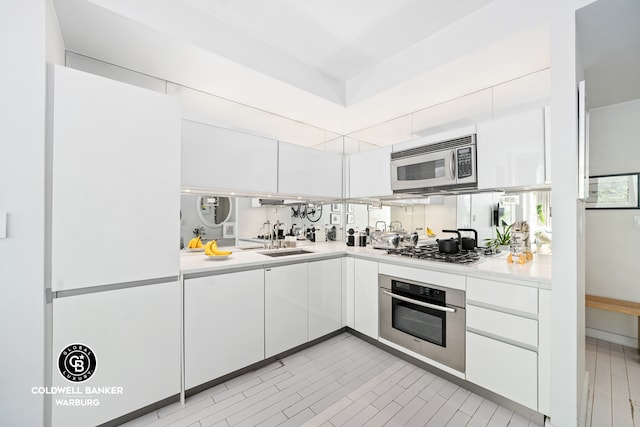 kitchen featuring a sink, appliances with stainless steel finishes, white cabinets, and light countertops