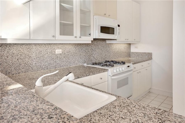 kitchen with a sink, backsplash, white appliances, white cabinets, and light tile patterned floors