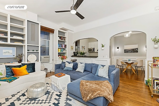 living area with visible vents, a ceiling fan, built in features, wood finished floors, and arched walkways