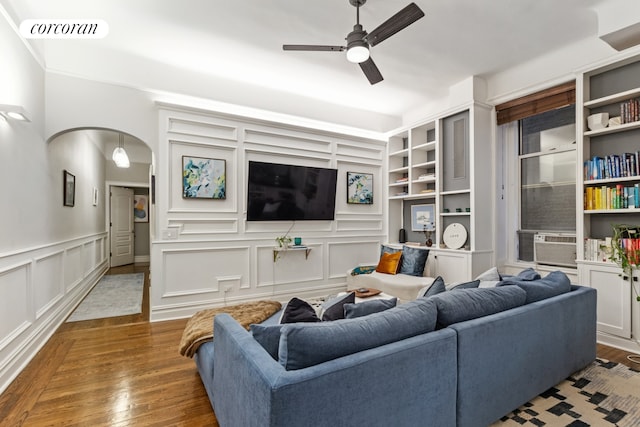 living room featuring visible vents, ceiling fan, wood finished floors, arched walkways, and a decorative wall