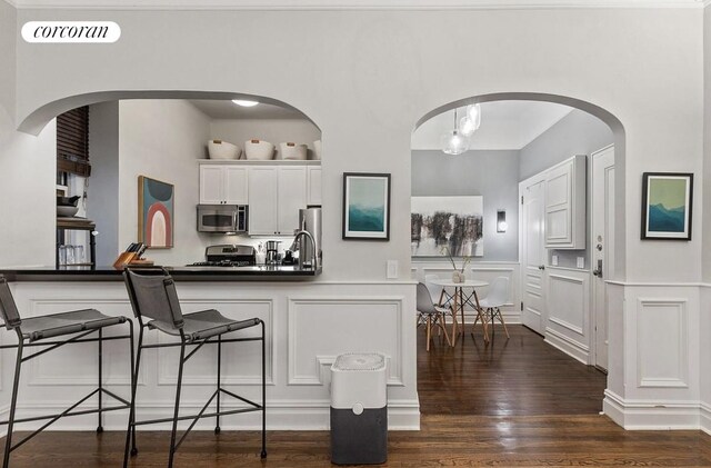 kitchen with visible vents, dark wood-type flooring, a kitchen bar, appliances with stainless steel finishes, and white cabinets