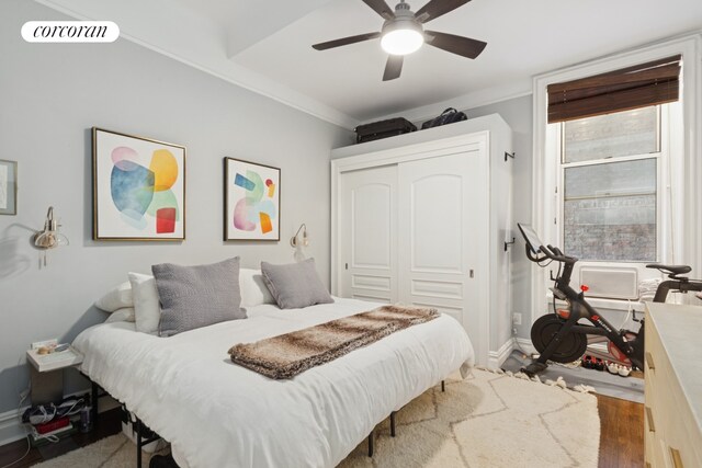 bedroom featuring a ceiling fan, wood finished floors, baseboards, a closet, and ornamental molding