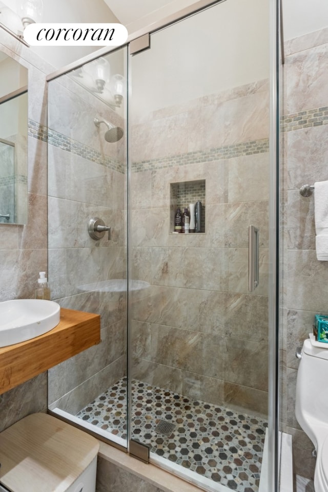 bathroom with a sink, tile walls, a shower stall, and toilet