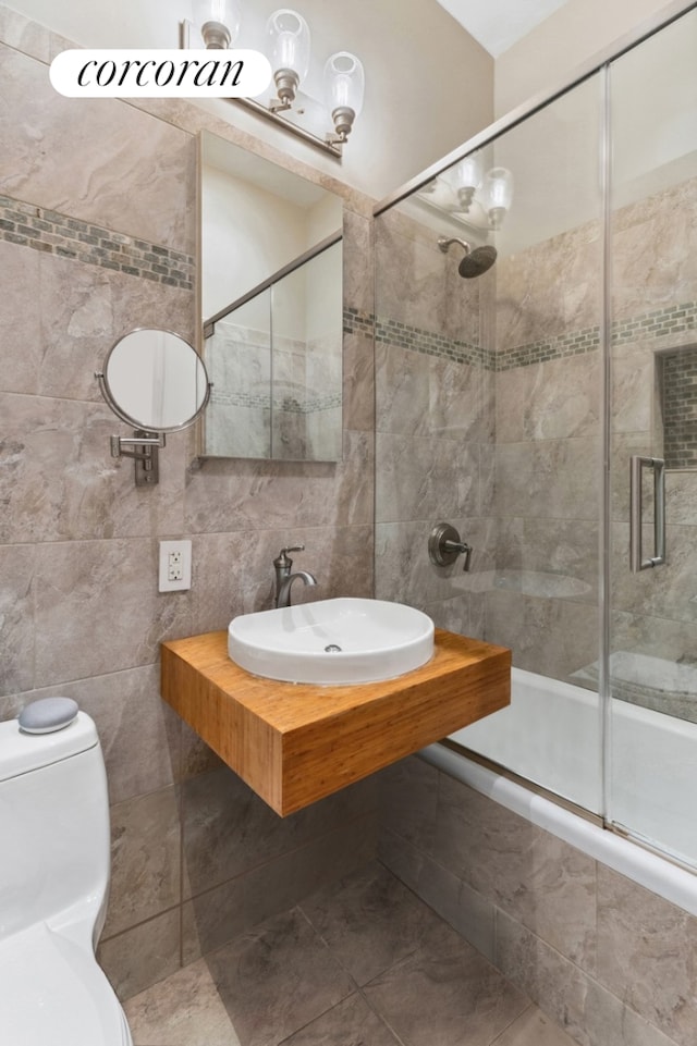 bathroom with tile walls, tile patterned flooring, a sink, toilet, and tiled shower / bath combo