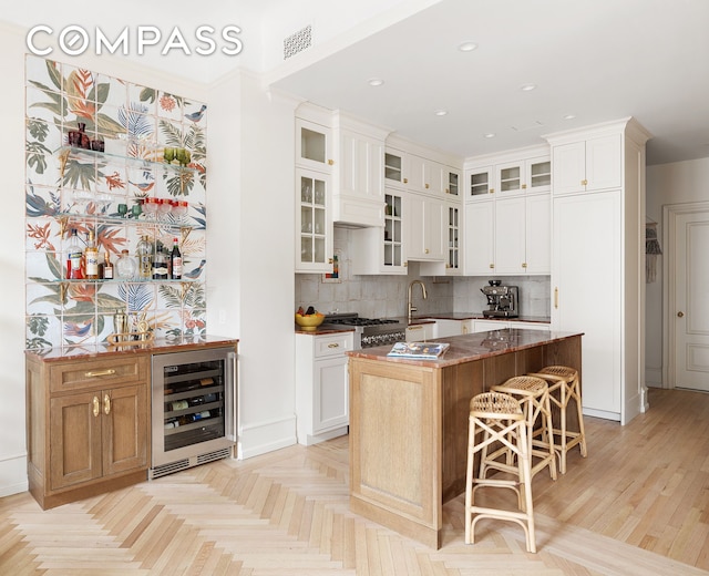 kitchen with decorative backsplash, an island with sink, beverage cooler, and a kitchen bar