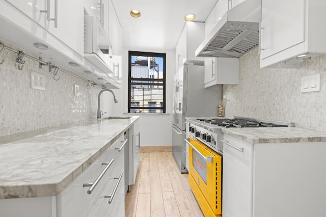 kitchen featuring high end range, range hood, white cabinets, and a sink