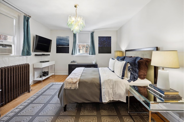 bedroom featuring an inviting chandelier, radiator, wood finished floors, and baseboards