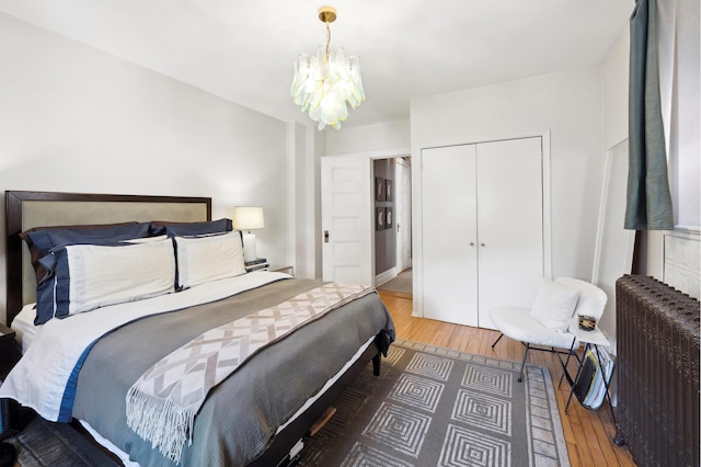 bedroom featuring a notable chandelier, radiator, wood finished floors, and a closet