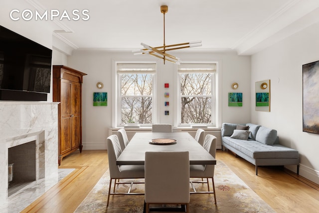 dining area featuring baseboards, light wood-style flooring, a high end fireplace, ornamental molding, and a notable chandelier