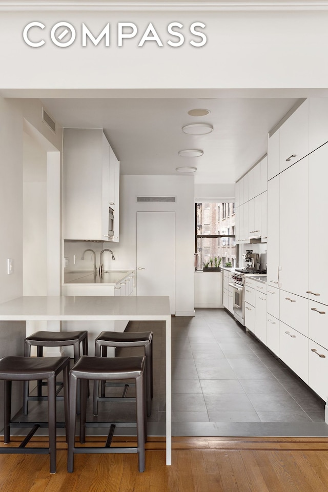 kitchen with visible vents, a peninsula, stainless steel stove, light countertops, and a kitchen bar