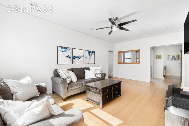 living area featuring baseboards, light wood-type flooring, and ceiling fan