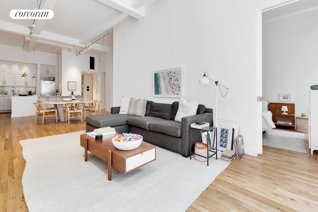 living area featuring beam ceiling, rail lighting, light wood-style floors, and a towering ceiling