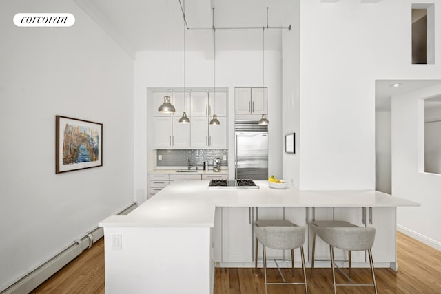 kitchen featuring a sink, stainless steel appliances, white cabinets, a baseboard heating unit, and backsplash