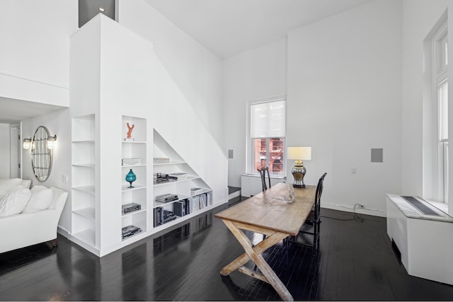 dining room featuring baseboards, dark wood-type flooring, and a towering ceiling