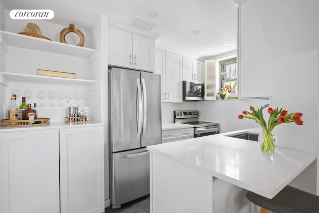 kitchen featuring a breakfast bar, open shelves, a peninsula, appliances with stainless steel finishes, and white cabinetry