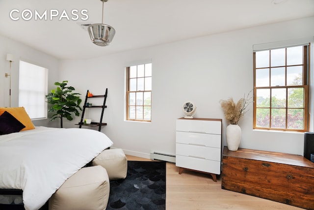 bedroom featuring light wood-style floors, baseboards, a baseboard radiator, and visible vents