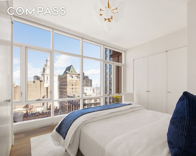 bedroom with wood finished floors, floor to ceiling windows, a closet, a city view, and a chandelier