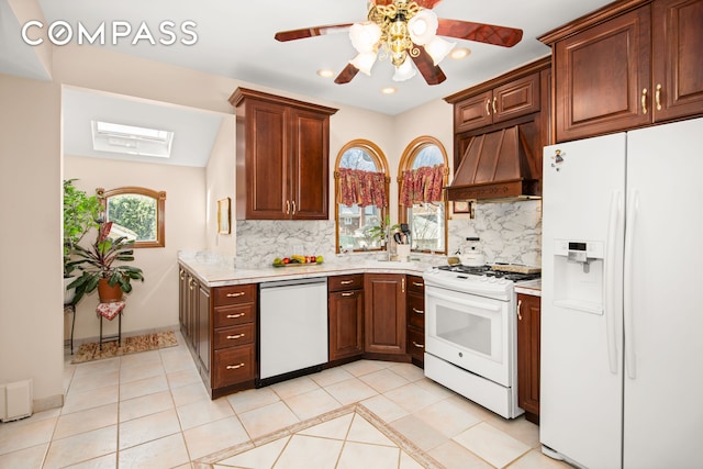 kitchen with white appliances, custom range hood, a skylight, and light countertops