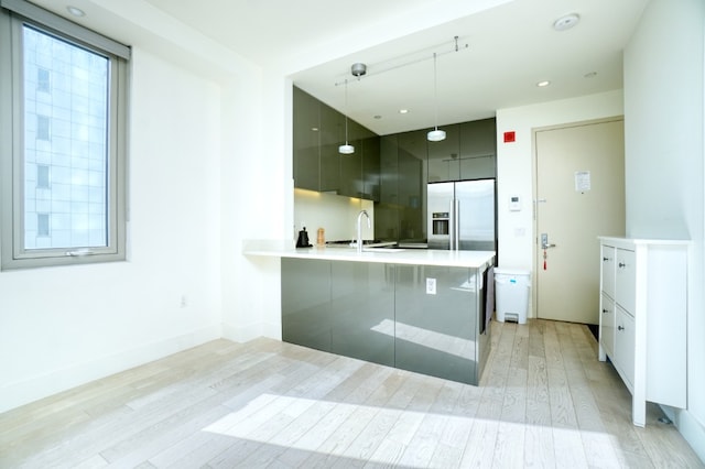 kitchen featuring stainless steel built in fridge, modern cabinets, a sink, a peninsula, and light wood finished floors