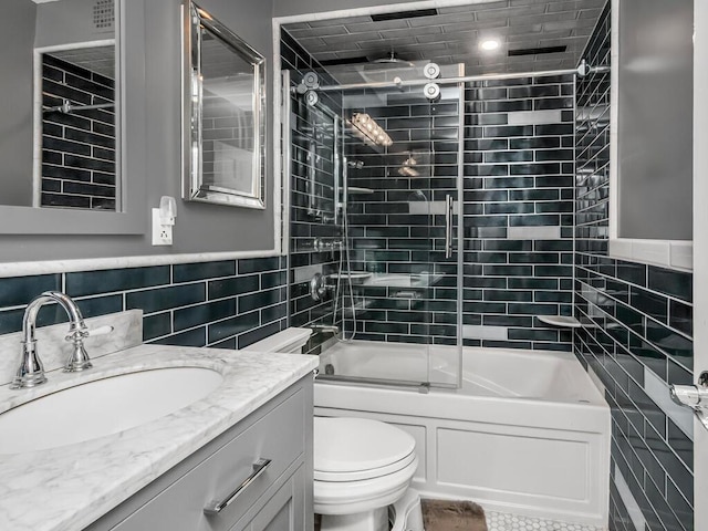 bathroom with a wainscoted wall, toilet, vanity, a combined bath / shower with rainfall shower, and tile walls