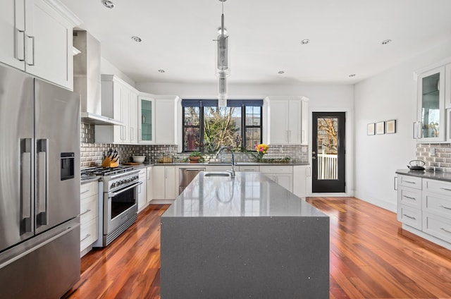 kitchen with high quality appliances, a sink, dark stone counters, wall chimney exhaust hood, and dark wood-style flooring