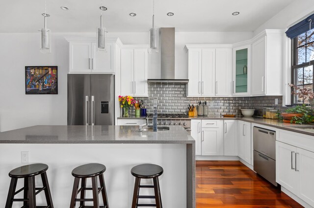 kitchen featuring backsplash, wall chimney range hood, a breakfast bar area, dark wood-style floors, and stainless steel appliances